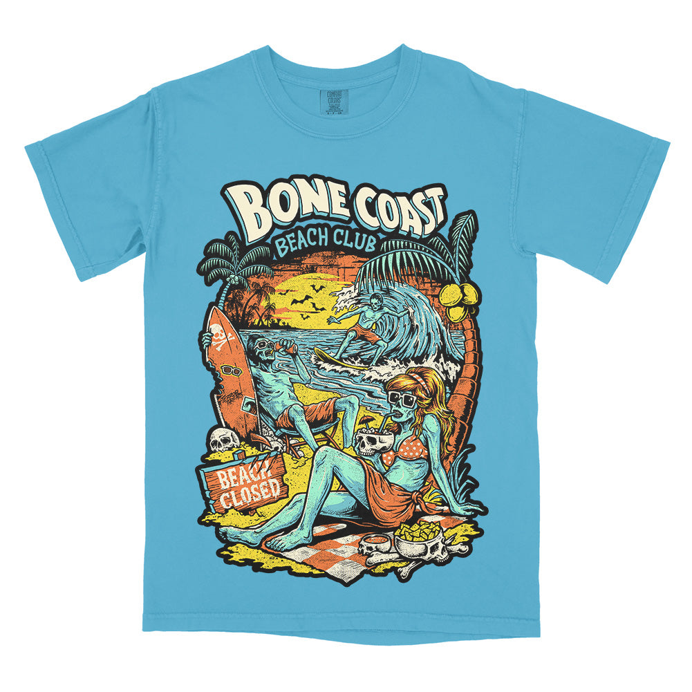 Bone Coast Beach Club sapphire Comfort Colors t-shirt featuring skeleton beachgoers, a surfer, palm trees, skulls, waves, and a beach closed sign in a retro tropical horror design.