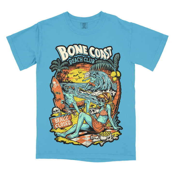 Bone Coast Beach Club sapphire Comfort Colors t-shirt featuring skeleton beachgoers, a surfer, palm trees, skulls, waves, and a beach closed sign in a retro tropical horror design.