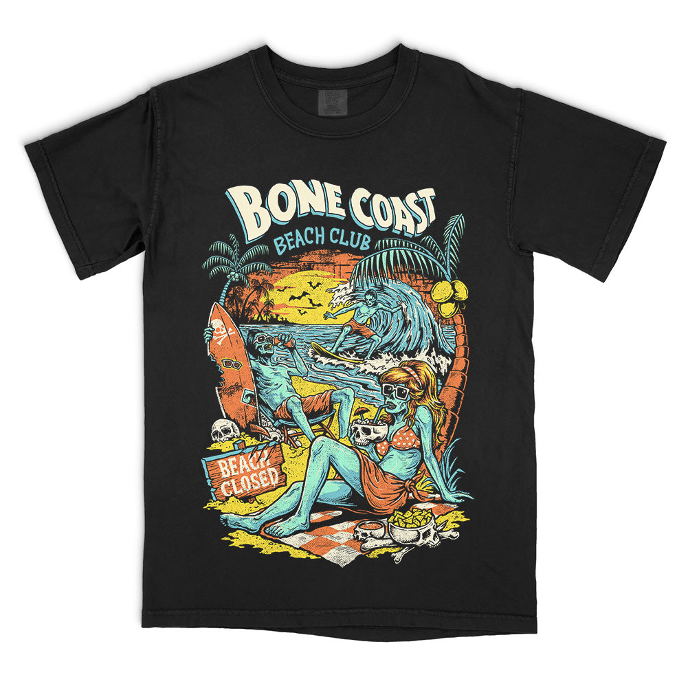 Bone Coast Beach Club black Comfort Colors t-shirt featuring skeleton beachgoers, a surfer, palm trees, skulls, waves, and a beach closed sign in a retro tropical horror design.